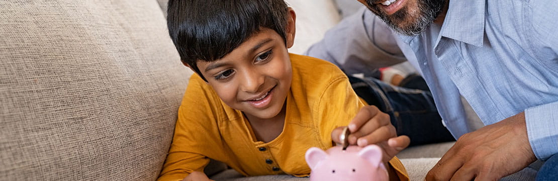 Happy indian son saving money in piggy bank with father